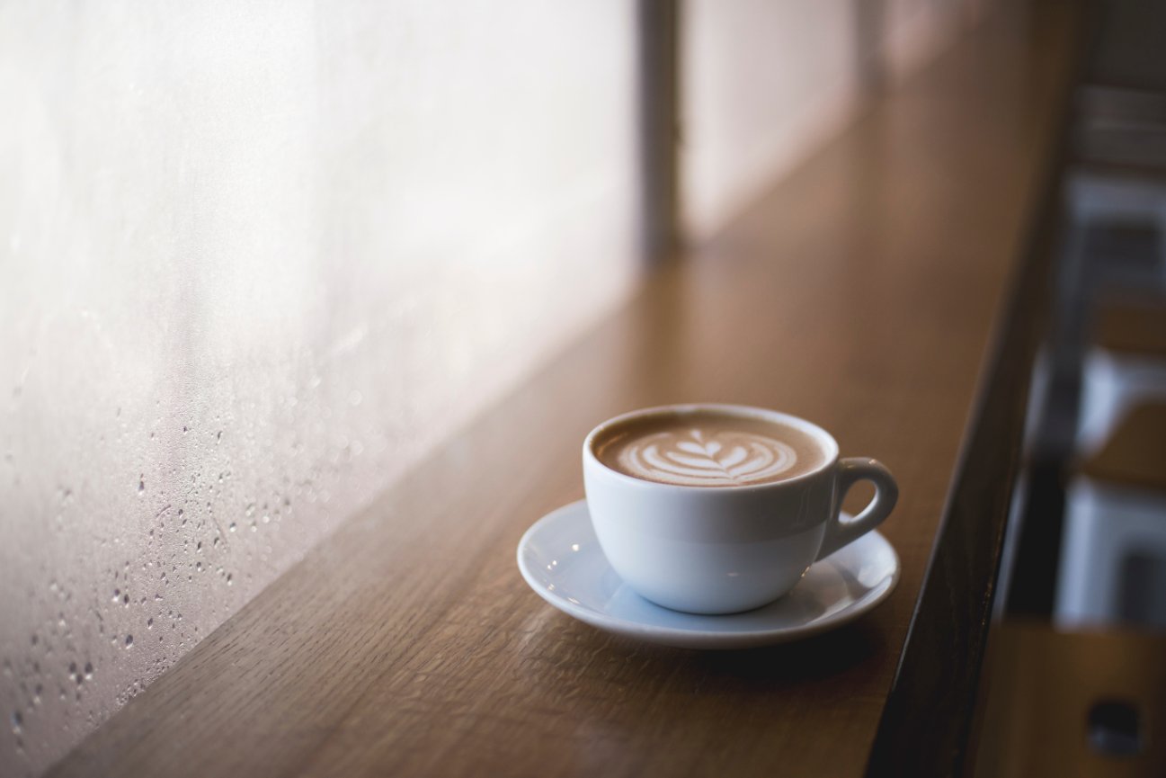 A cup of coffee on a wooden table with natural light in a cozy setting.
