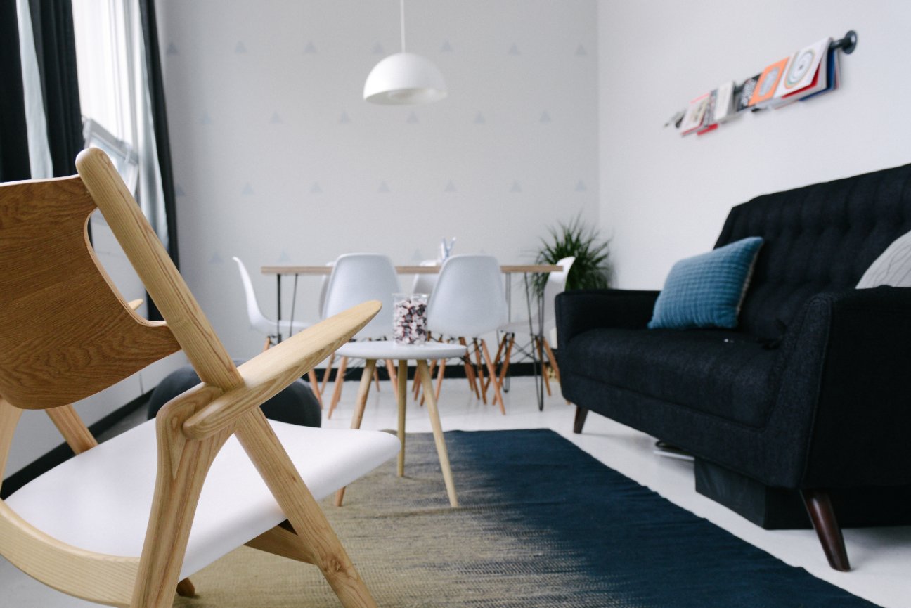 Modern living room with wooden chair, black sofa, dining table, and minimal decor.
