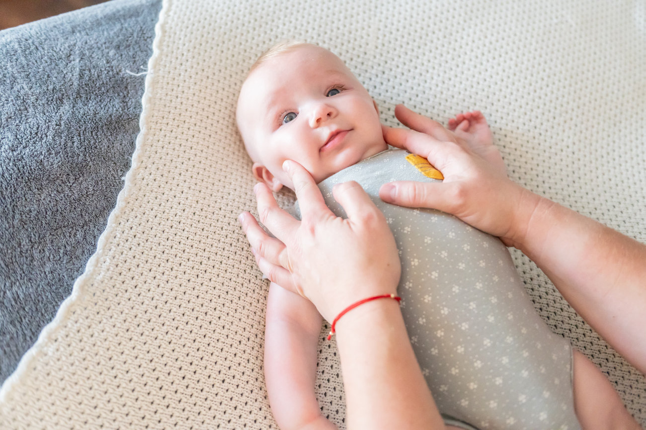 A baby lying face up smiling while Deandra gently helps with neck tension.